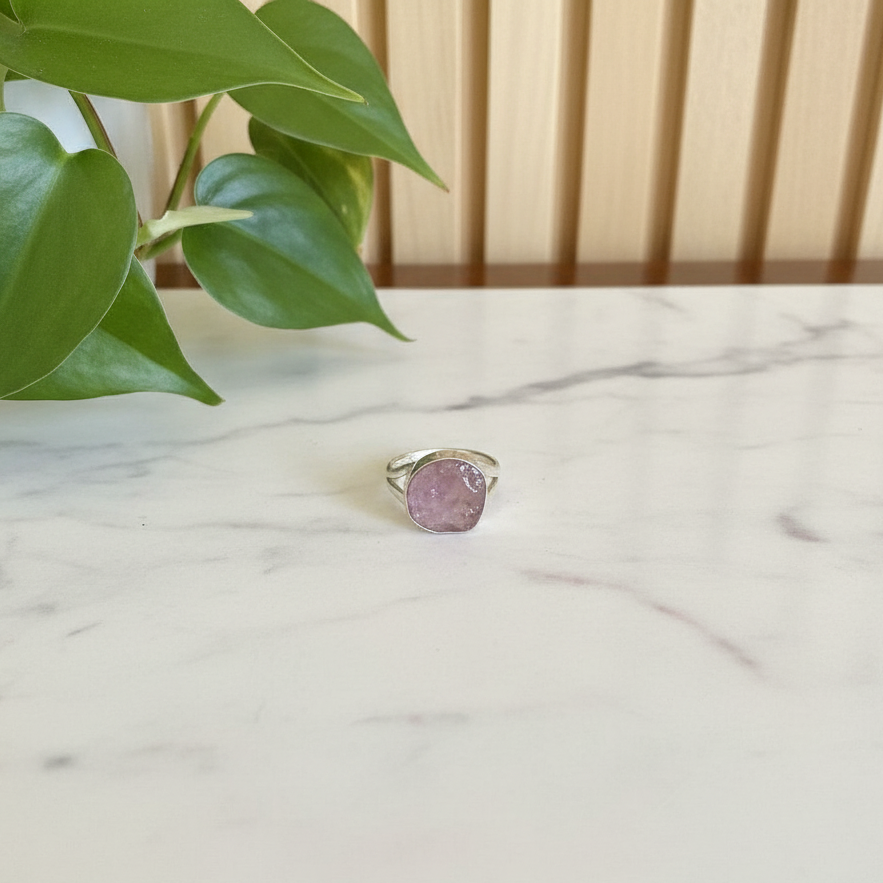 Pink gemstone ring on a marble surface with green leaves in the background