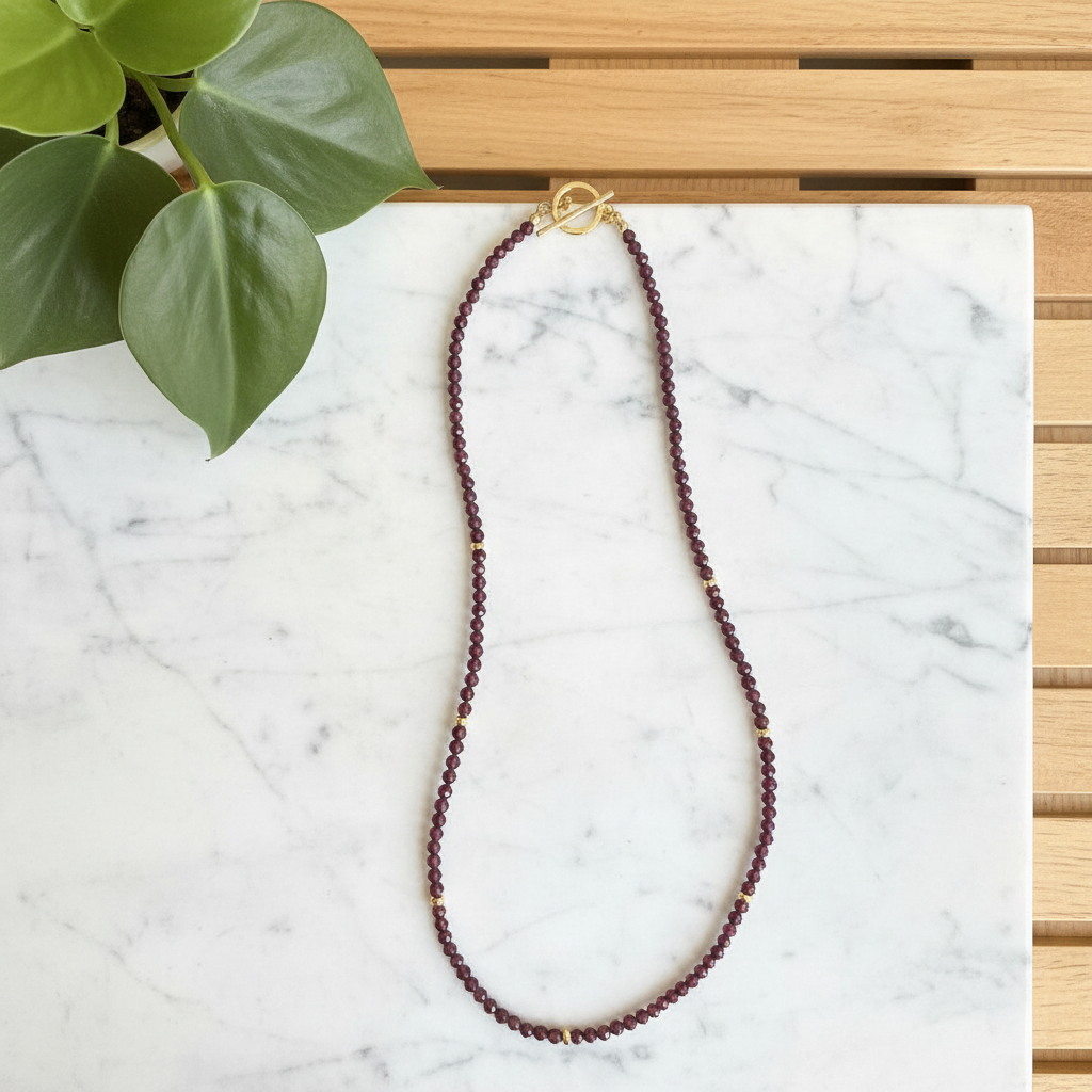 Red garnet beaded necklace on a white counter with a plant in the background
