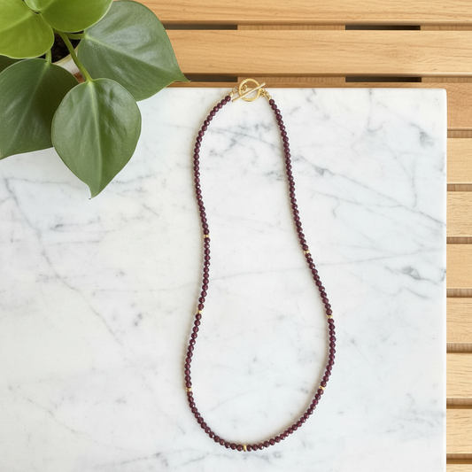 Red garnet beaded necklace on a white counter with a plant in the background