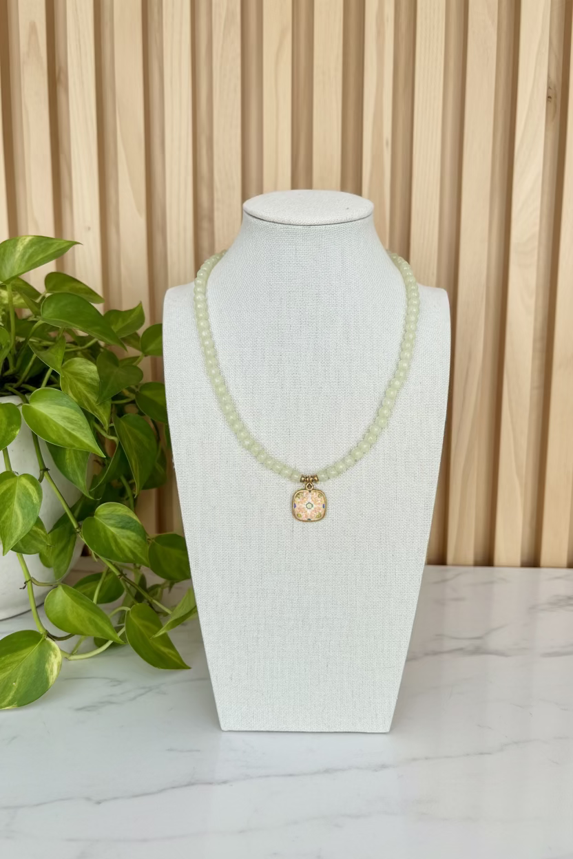 A yellow beaded necklace displayed on a white fabric mannequin bust, featuring a central square pendant with a gold-toned border
