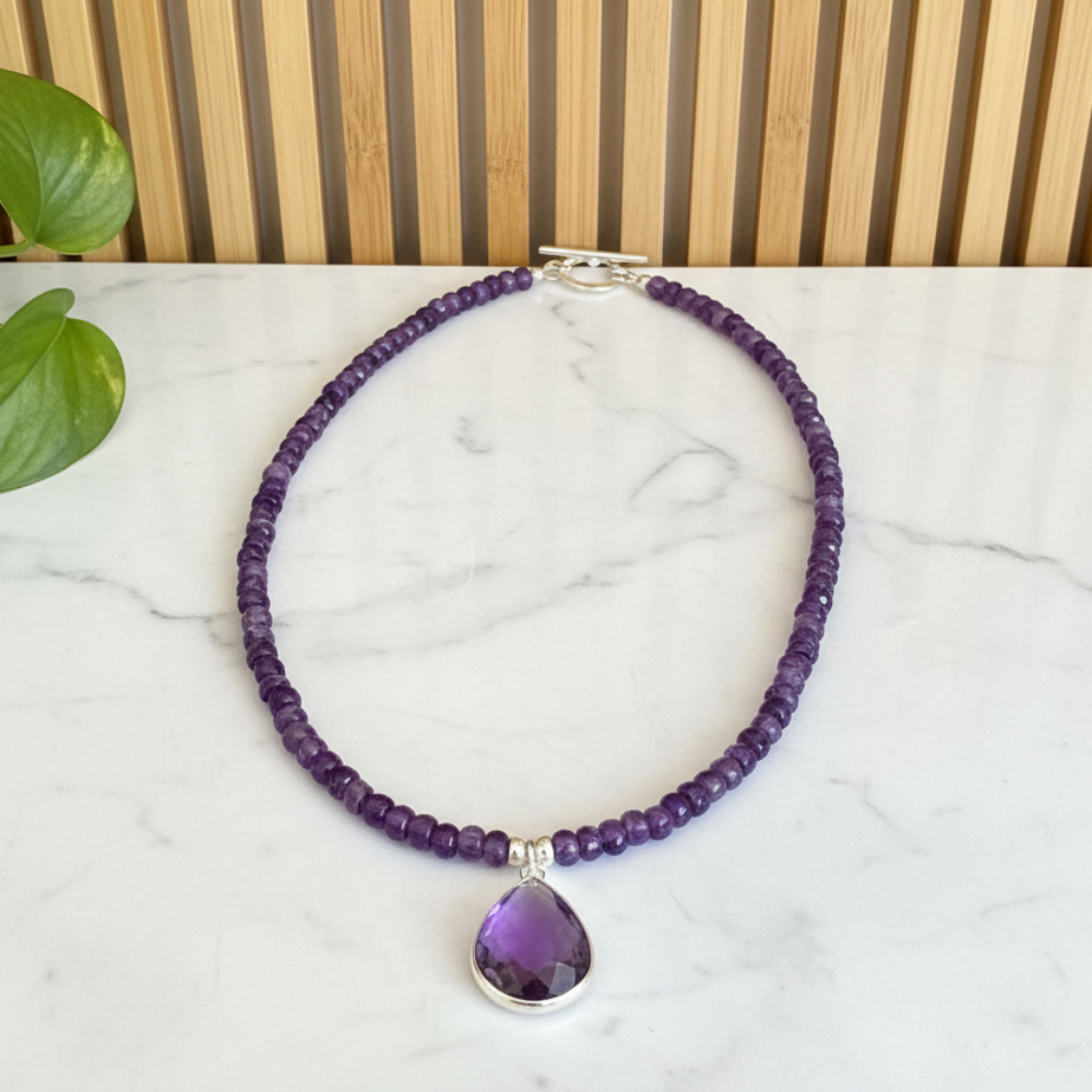 Purple amethyst beaded necklace with a teardrop pendant on a marble surface.