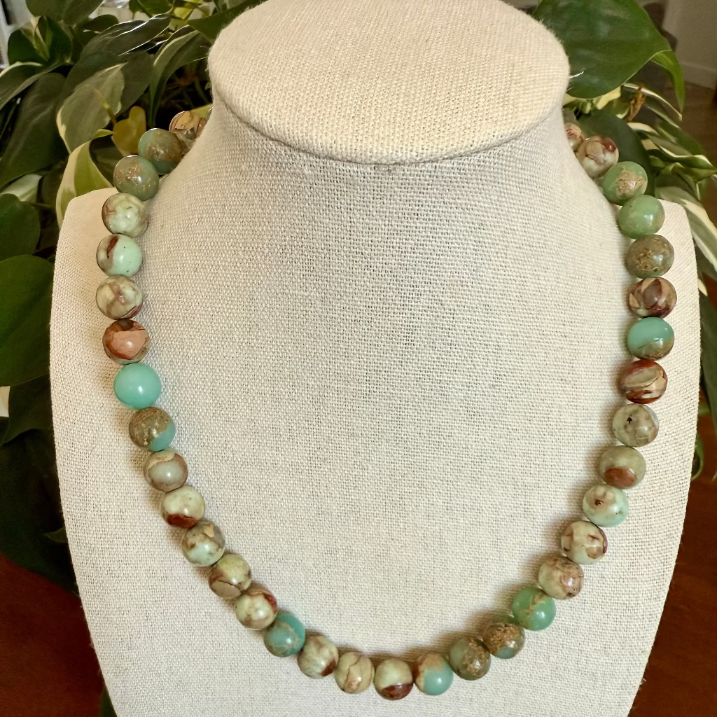 Necklace with green and brown beads on a white mannequin bust.