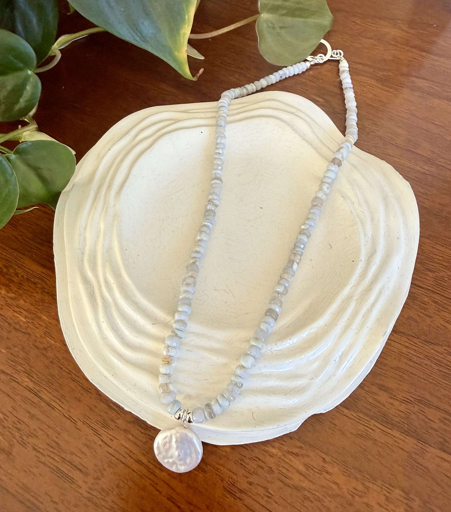 Necklace with a large pearl pendant on a white shell with green leaves in the background