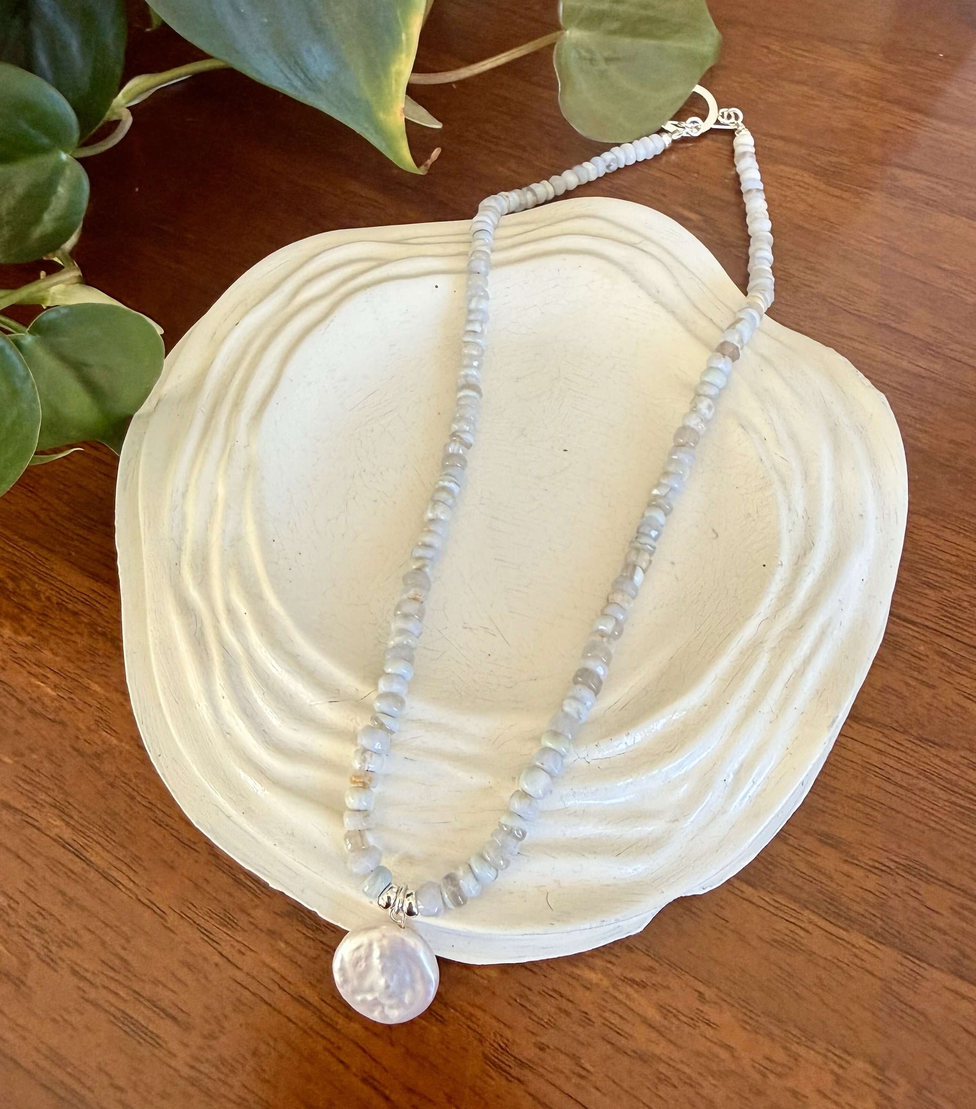 Necklace with a large pearl pendant on a white shell with green leaves in the background