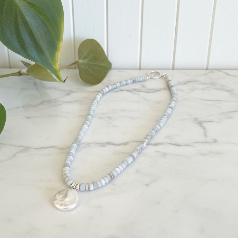Chalcedony beaded necklace with a pearl pendant on a white marble counter. 