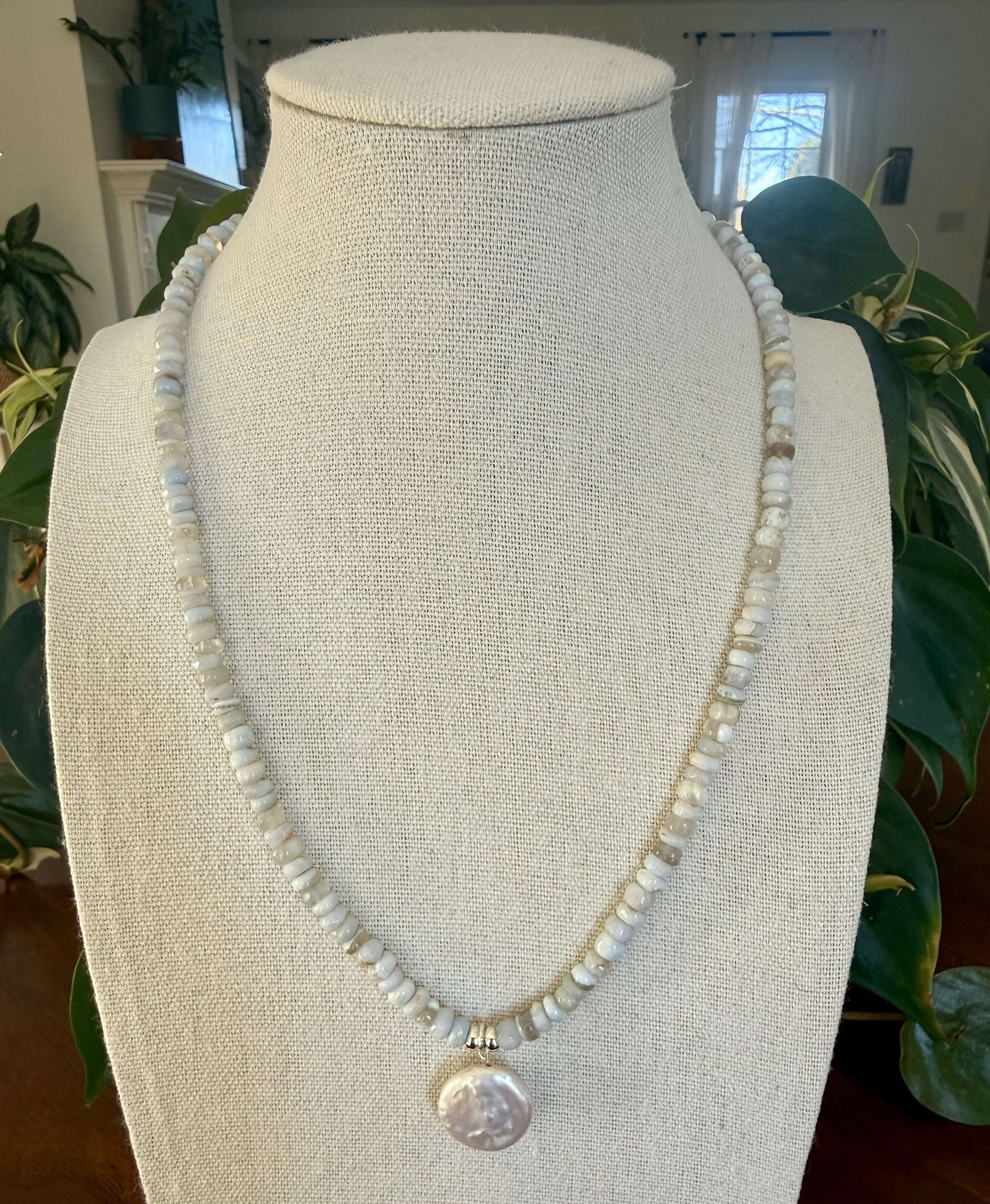 Pearl necklace on a mannequin bust with plants in the background