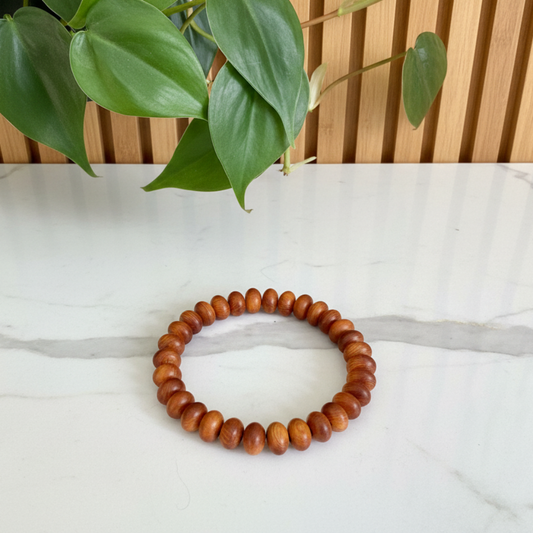 Wooden beaded bracelet on a white marble countertop with a plant in the background
