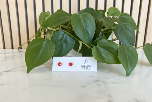Two red Jade stud earrings on a Willow & Fern card sitting on a white marble counter with a plant in the background