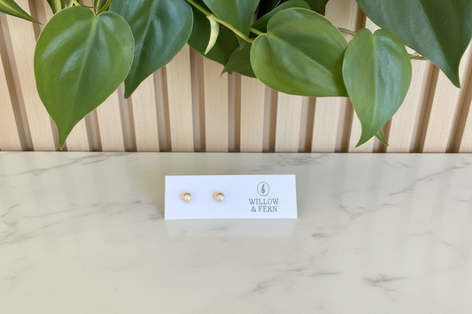 Two off white pearl earrings on a Willow & Fern card sitting on a white marble counter with a plant in the background