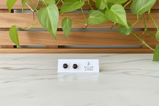 Two black stud tourmaline earrings on a Willow & Fern card sitting on a marble counter with a plant in the background