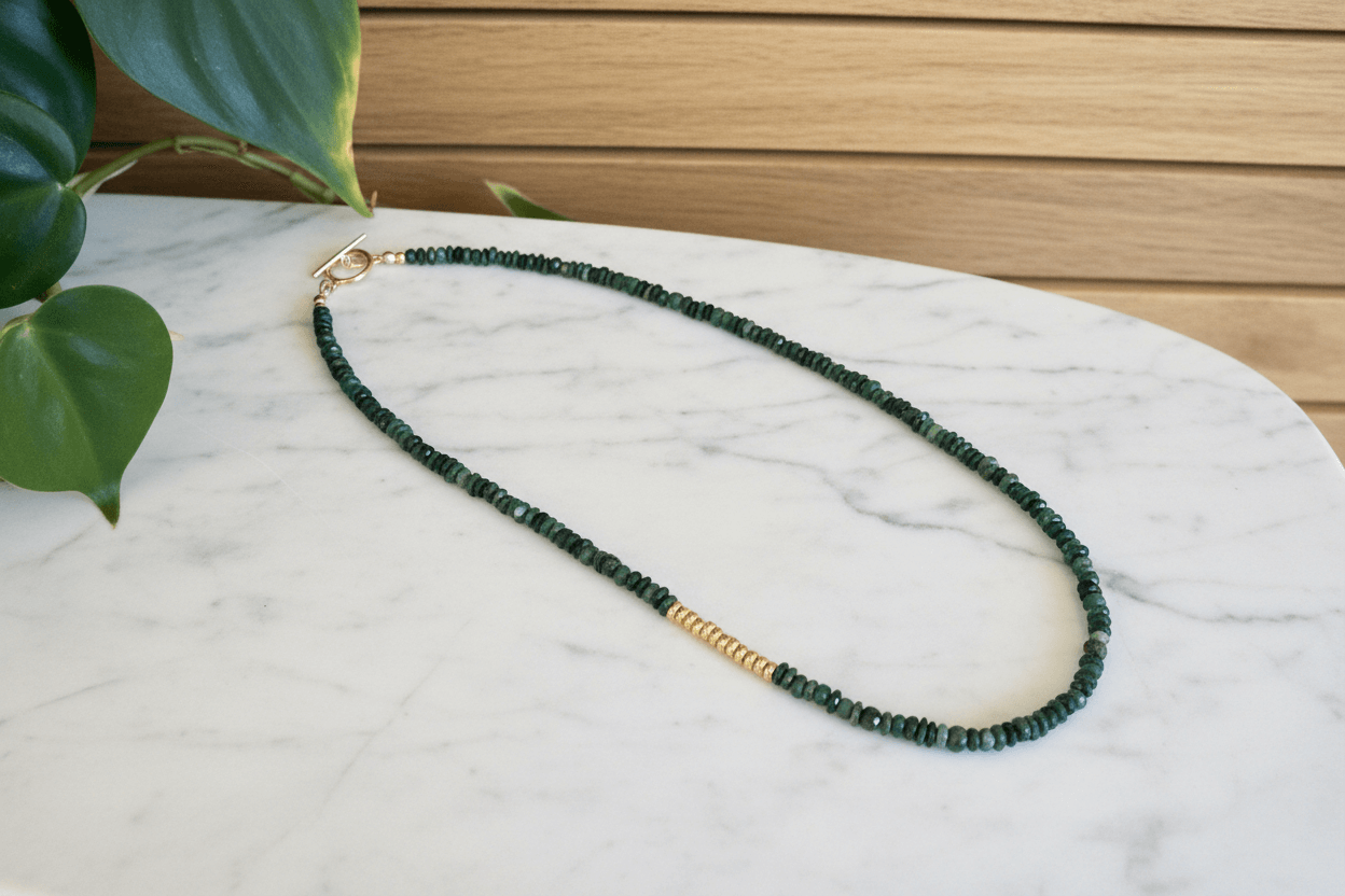 Green emerald beaded necklace with gold spacers on a marble surface with a wooden background