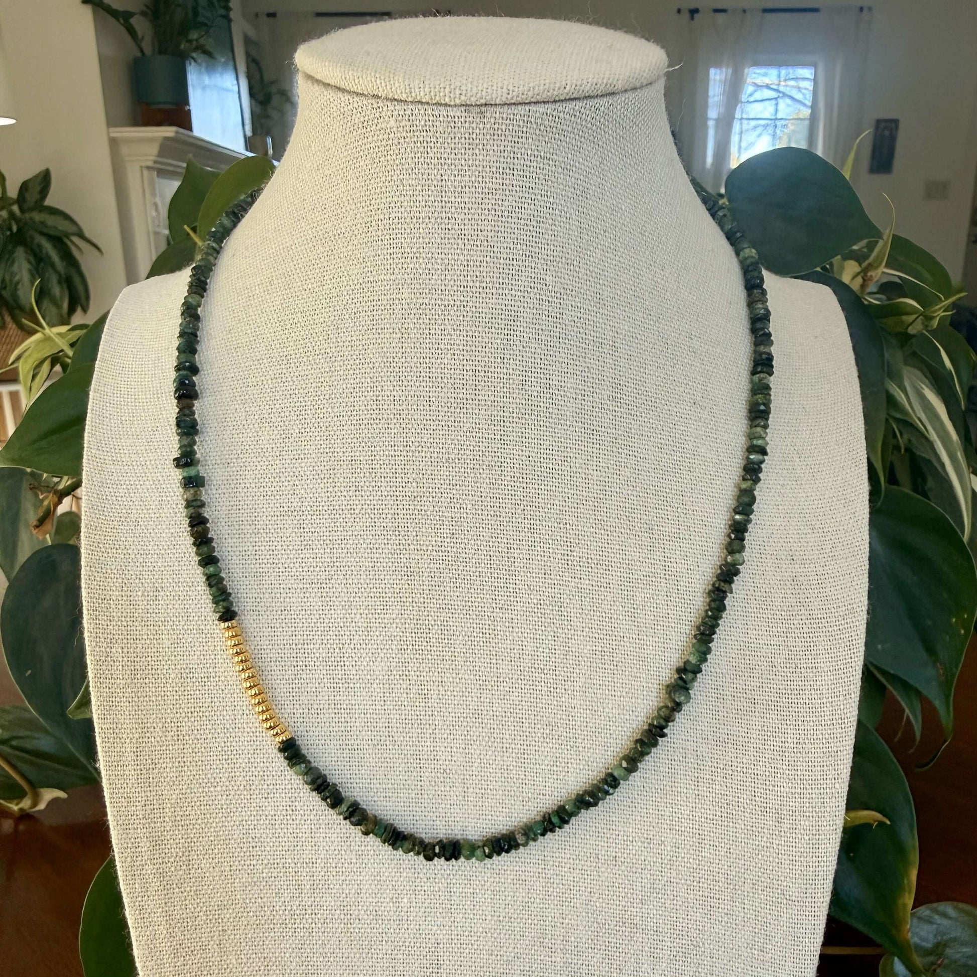 Green emerald beaded necklace with gold spacers on a mannequin bust with plants in the background