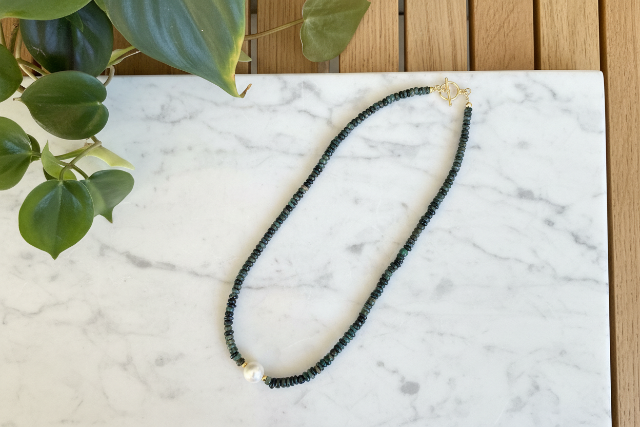 Necklace with green emerald beads and a pearl on a white marble background