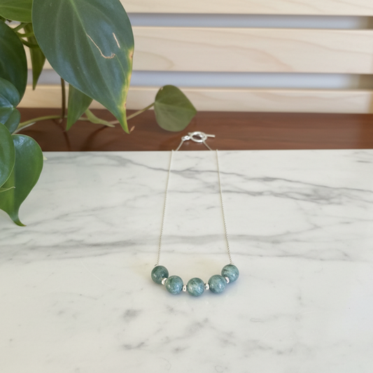 Jade beads on a silver necklace sitting on a white marble background