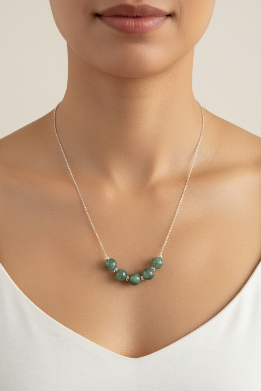 Necklace with green jade beads worn by a person on a neutral background