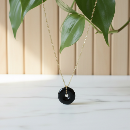 Necklace with a dark green jade pendant on a white surface with a plant in the background