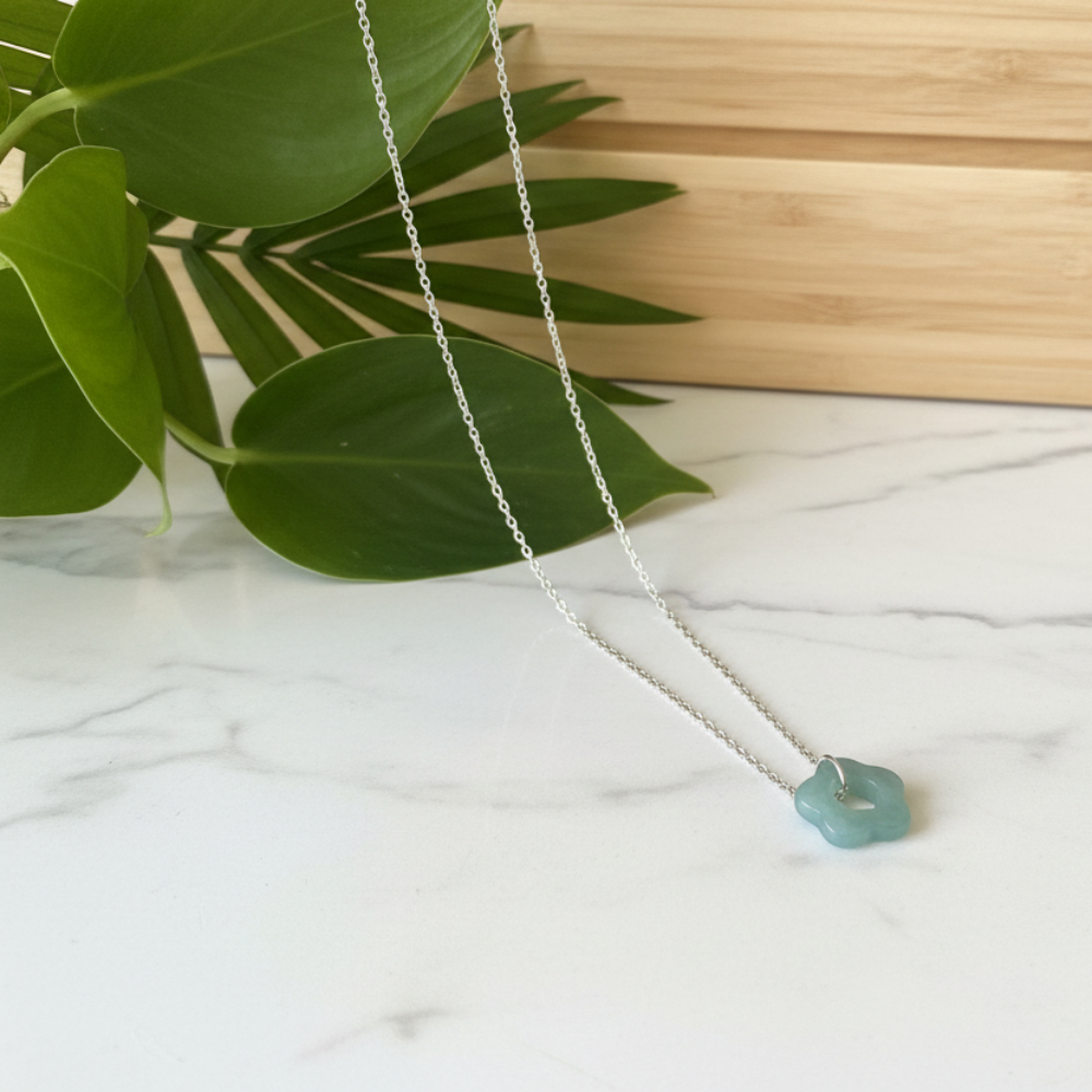 Green Jade necklace on a white marble surface with green leaves and a wooden background 
