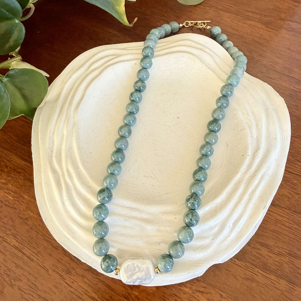 Green jade beaded necklace on a white shell with leaves in the background