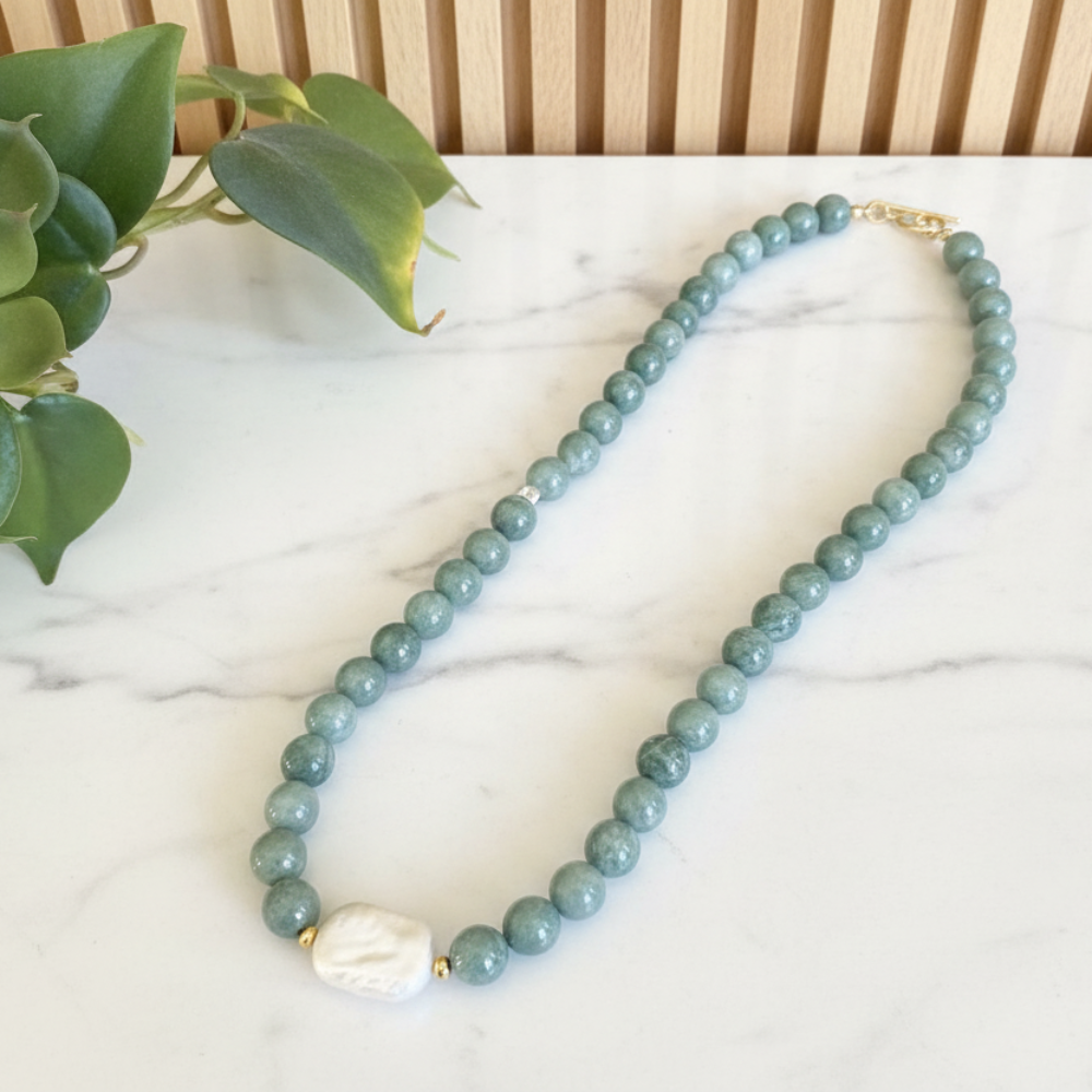Green jade beaded necklace on a white marble counter with leaves in the background