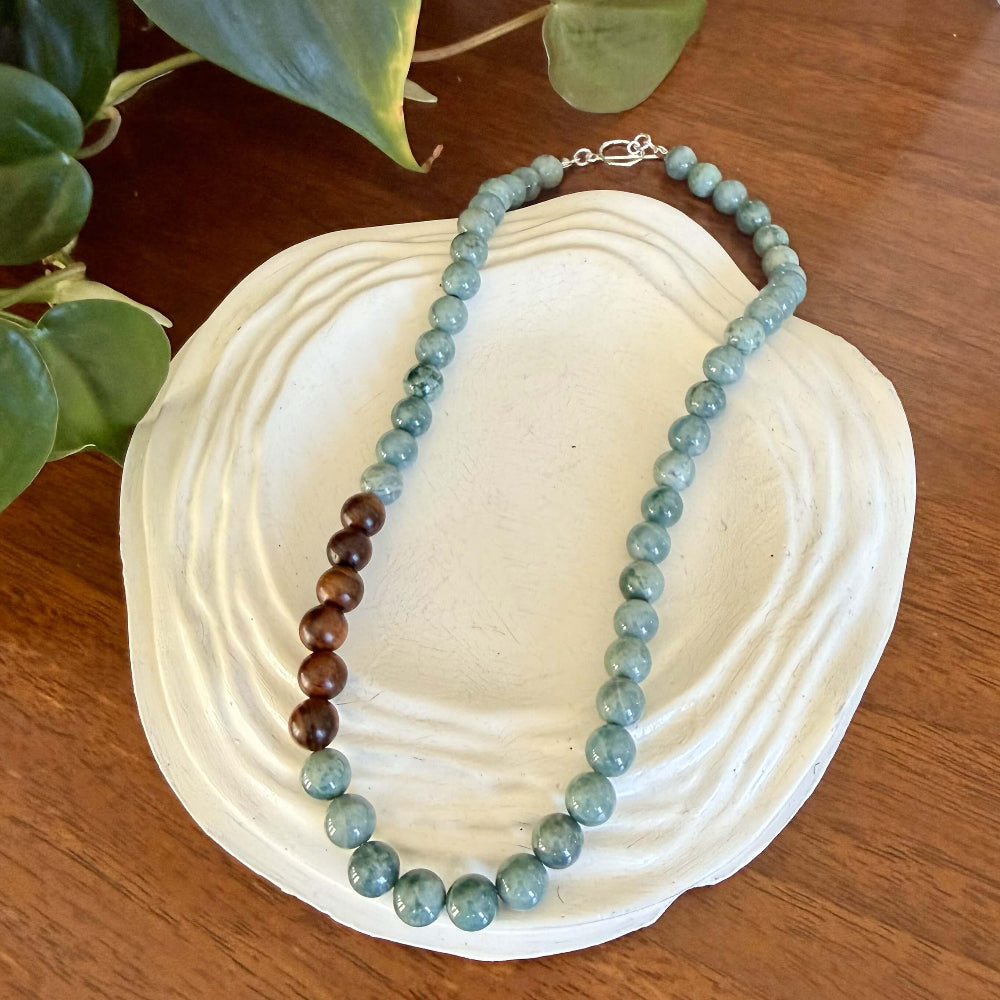 Necklace with jade and wooden beads on a white stone surface with green leaves in the background
