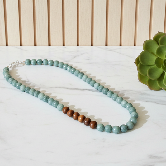 Jade and wooden beaded necklace on a white marble surface with a green plant in the background.