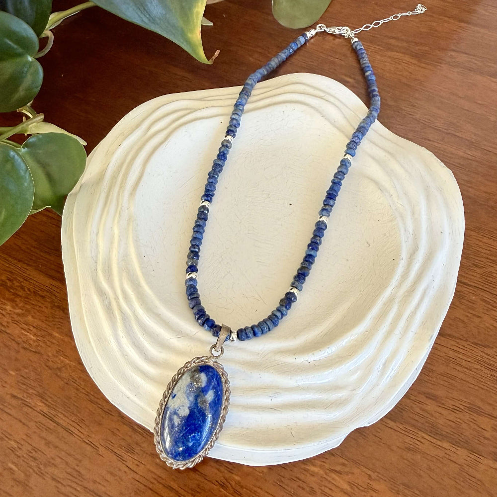 Blue lapis lazuli beaded necklace with a pendant on a white dish on a wooden surface