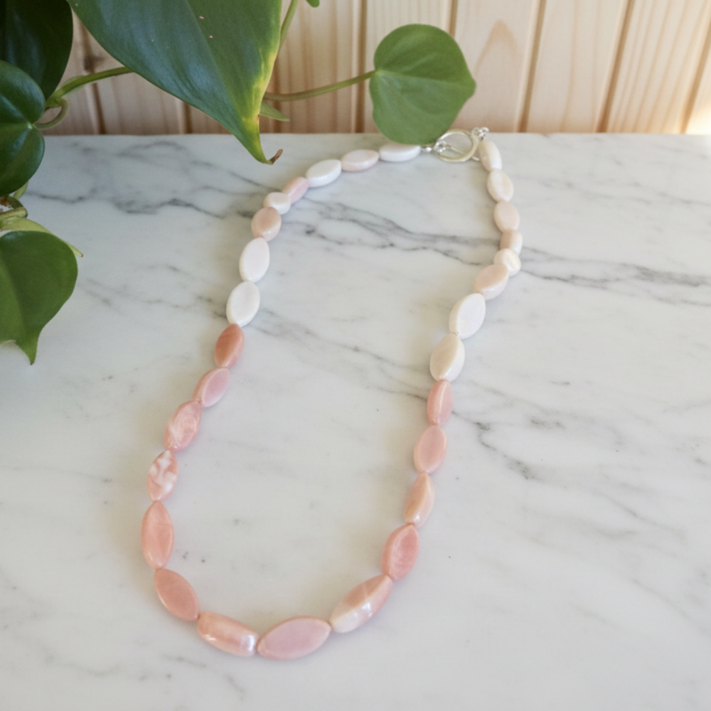 Necklace with pink opal beads with pink and white colors on a marble surface with green leaves in the background