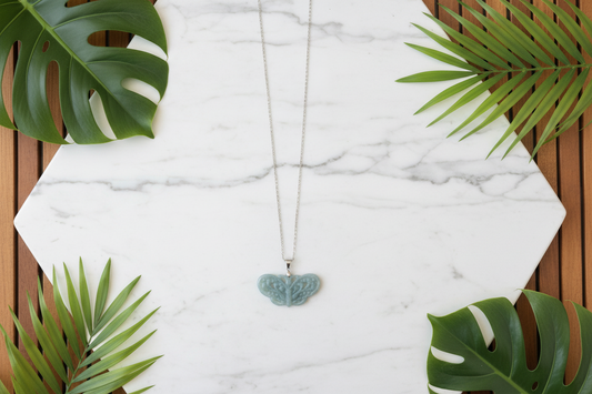 Butterfly pendant on a white marble counter with plants in the background