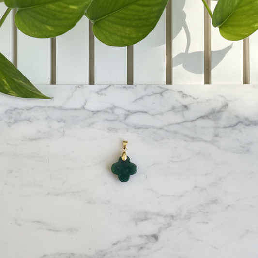 White marble counter with a green plant and dark green jade clover pendant with a gold bail