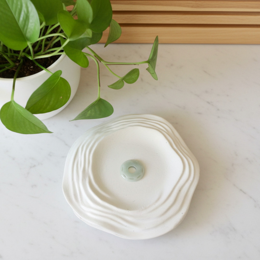 Light green jade pendant on a white ceramic dish with a green plant in the background