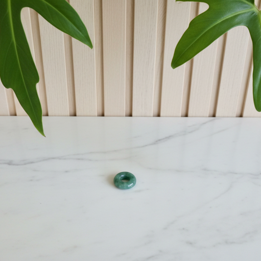 White marble counter with a dark green jade donut pedant with a plant in the background