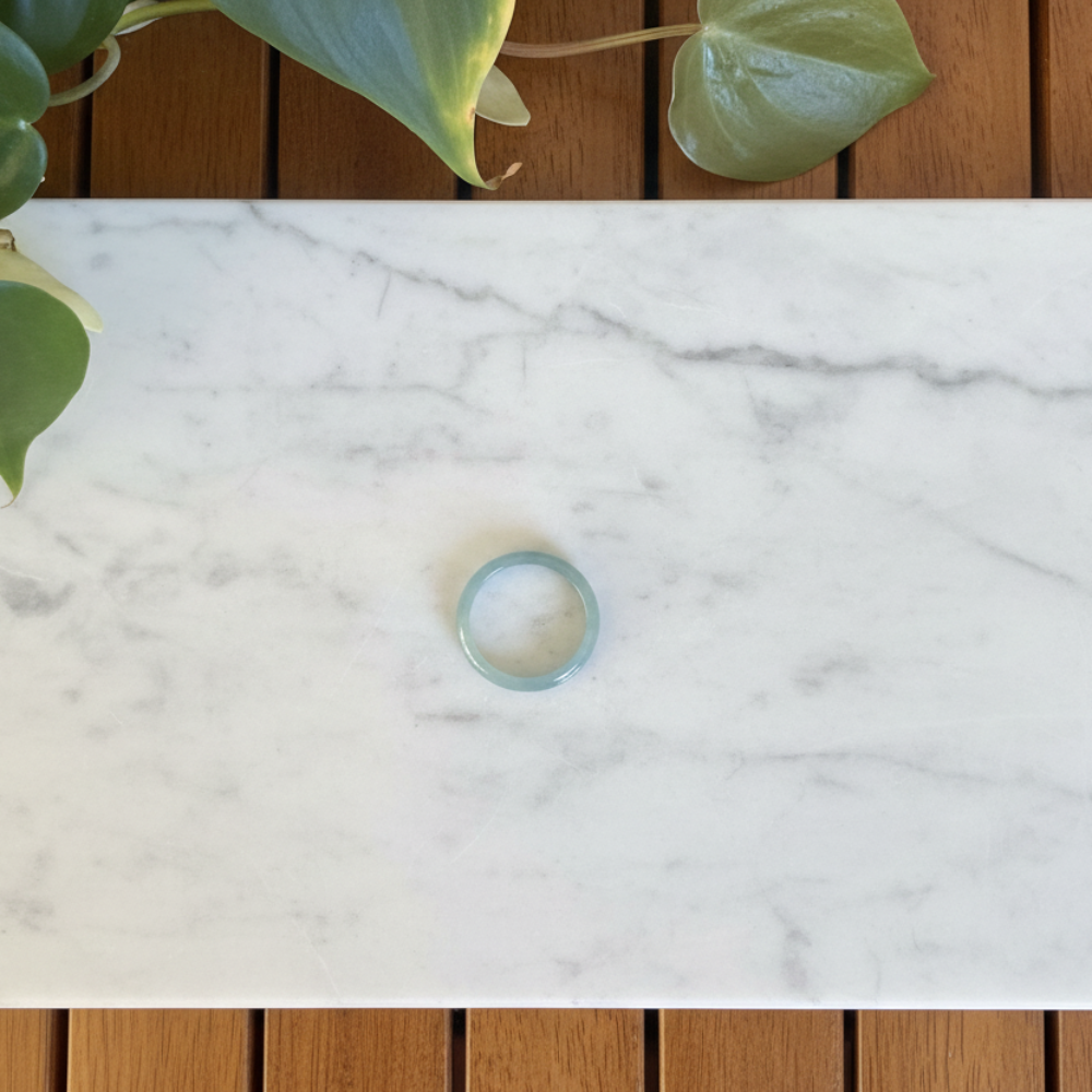 Thin green jade ring on a marble counter with a plant in the background