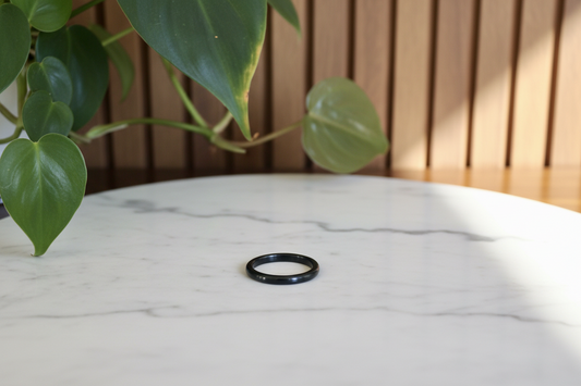 Thin black jade ring on a marble counter with a plant in the background