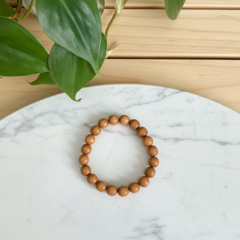 Light sandalwood beaded bracelet on a textured white dish with green leaves in the background