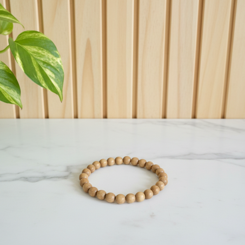 Light sandalwood beaded bracelet on a white marble counter with green leaves in the background