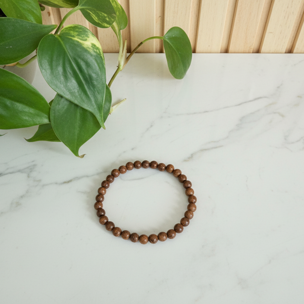 Sandalwood small beaded bracelet on a white countertop with green leaves in the background
