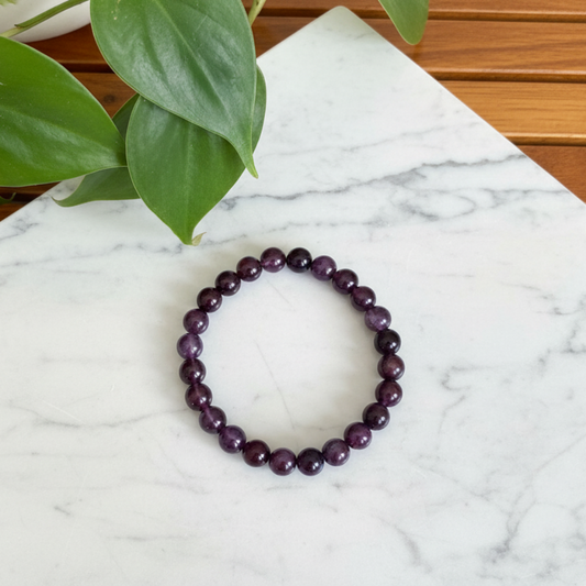 Purple Sandalwood beaded bracelet on a white countertop with a plant in the background