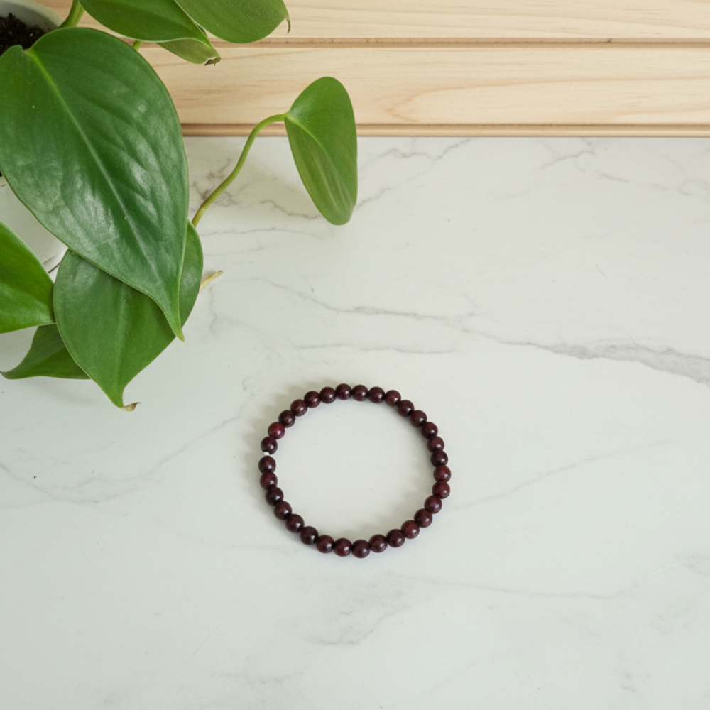 Purple sandalwood beaded bracelet on a white marble counter with green leaves in the background